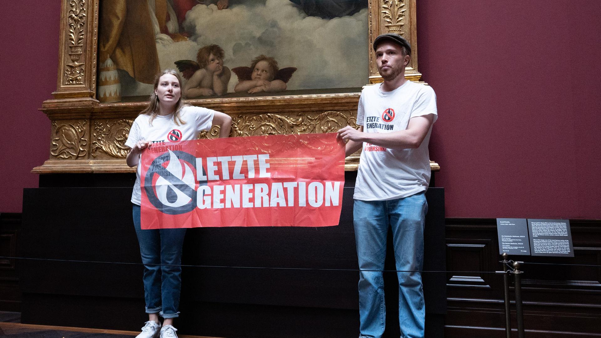 Sachsen, Dresden: Zwei Umweltaktivisten der Gruppe "Letzte Generation" stehen mit einem Banner in der Gemäldegalerie Alte Meister an dem Gemälde "Sixtinische Madonna" von Raffael. Sie haben jeweils eine Hand am Rahmen des Bildes geklebt.