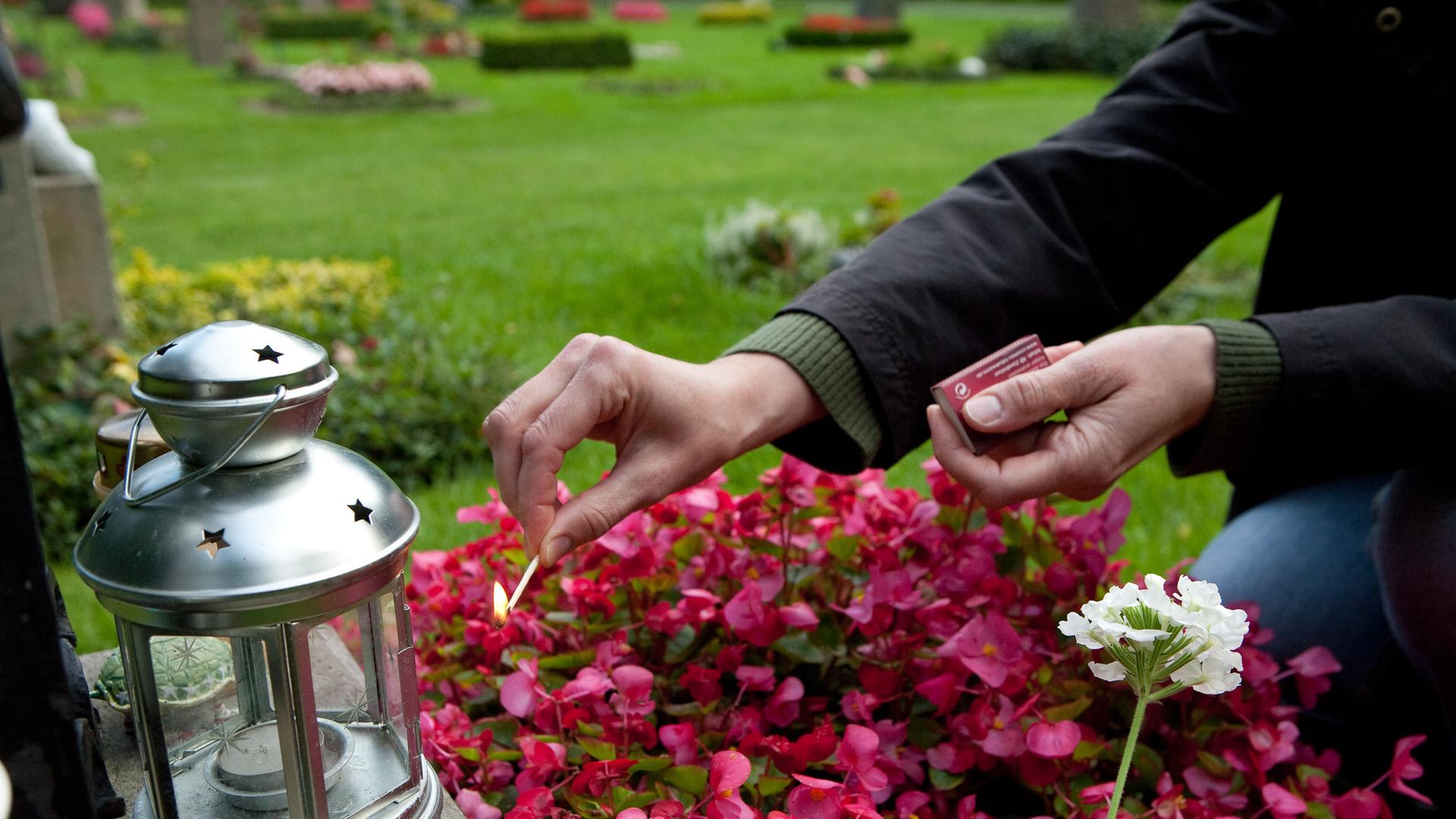 Schwerer Verlust: Auf einem Friedhof zünden Angehörige eine Kerze an, links im Bild ein Grablicht. Schwerer Verlust: Auf einem Friedhof zünden Angehörige eine Kerze an, links im Bild ein Grablicht.