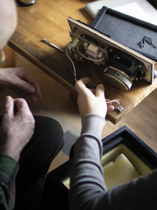 Zwei Männer sitzen vor einem ausgebauten Lautsprecher 