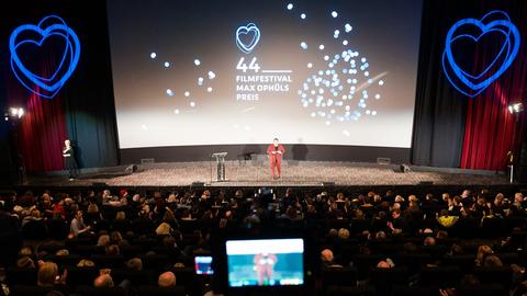 Die Bühne bei der Eröffnung des 44. Filmfestival Max Ophüls Preis, umgeben von Publikum. Im Hintergrund eine Projektion mit Herzen und dem Schriftzug "44. Filmfestival Max Ophüls Preis"