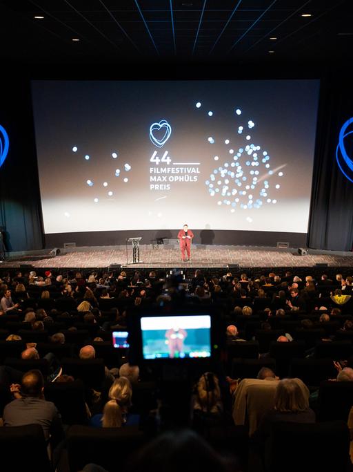 Die Bühne bei der Eröffnung des 44. Filmfestival Max Ophüls Preis, umgeben von Publikum. Im Hintergrund eine Projektion mit Herzen und dem Schrfitzug "44. Filmfestival Max Ophüls Preis"