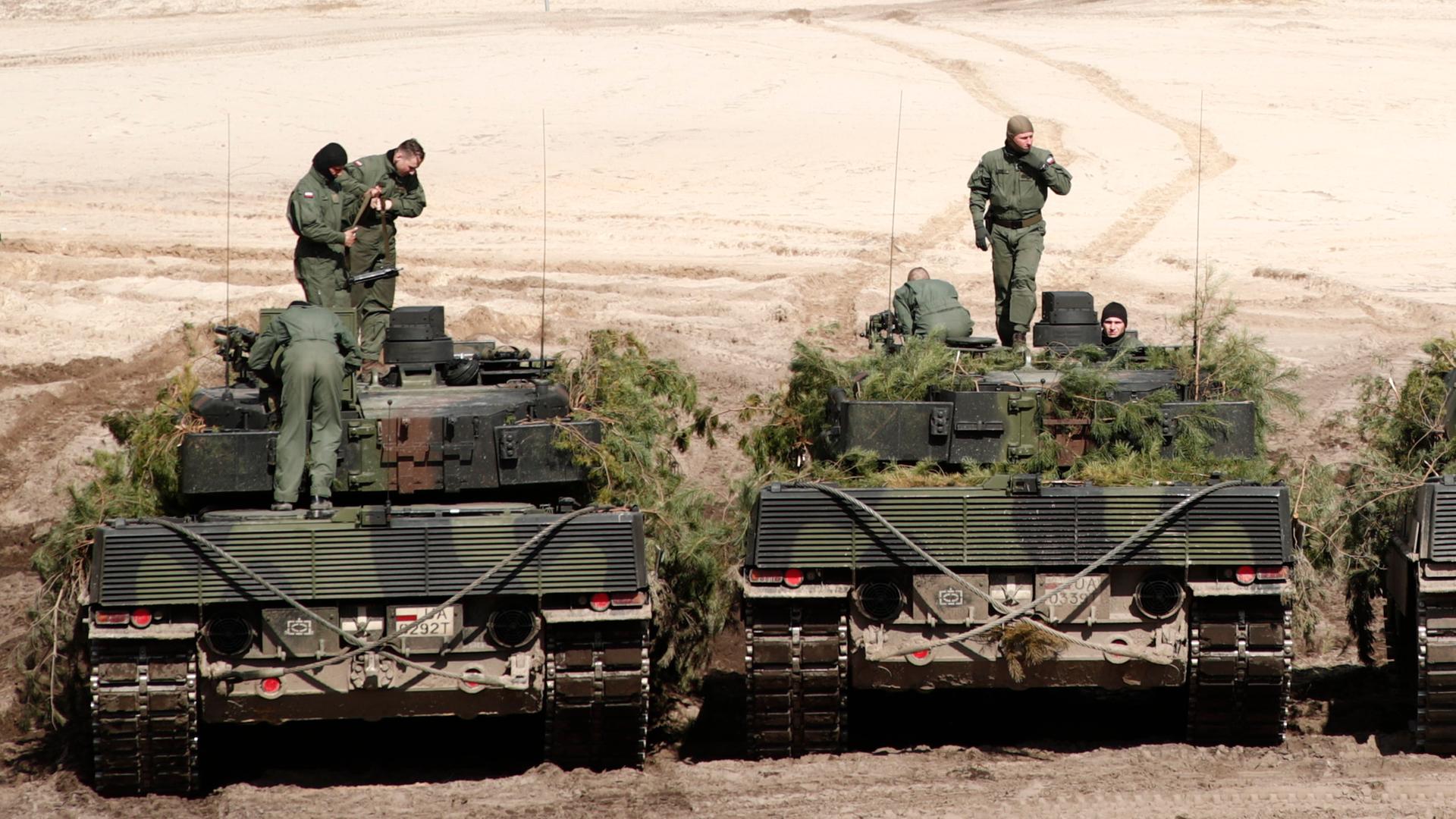Zwei Leopard-2-Panzer mit jeweils drei Soldaten stehen nebeneinander.