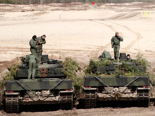 Zwei Leopard-2-Panzer mit jeweils drei Soldaten stehen nebeneinander.