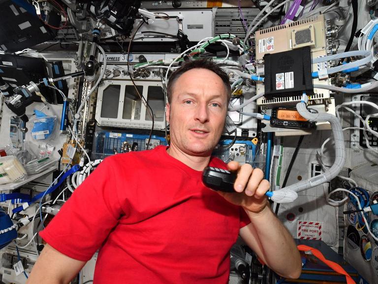 Matthias Maurer inmitten von Technik mit einem Mikron an der Hand an Bord der ISS