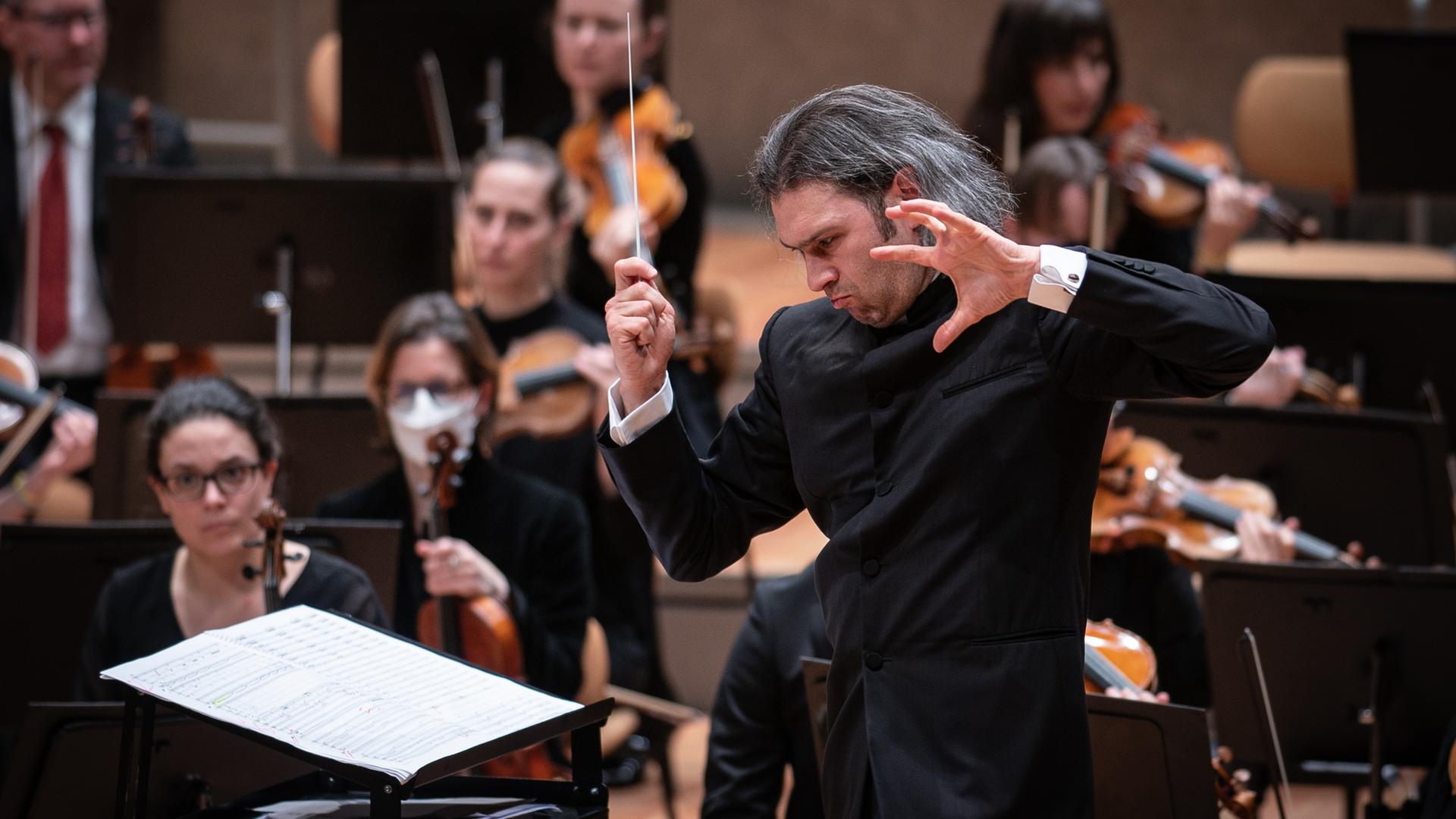 Der Dirigent Vladimir Jurowski steht mit offenen Haaren und kraftvoller Geste vor seinem Orchester. Der Dirigent Vladimir Jurowski steht mit offenen Haaren und kraftvoller Geste vor seinem Orchester.