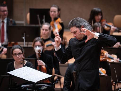 Der Dirigent Vladimir Jurowski steht mit offenen Haaren und kraftvoller Geste vor seinem Orchester.