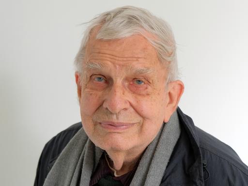 Der 84 Jahre alte Tomas Venclova schaut in die Kamera. Er hat weiße Haare, trägt eine dunkle Jacke und hat ein hellgraues Tuch um den Hals gelegt.