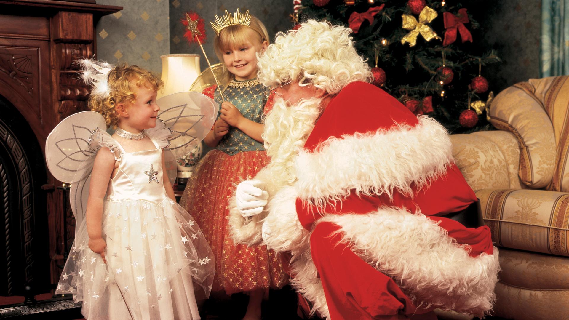 Ein verkleideter Weihnachtsmann und zwei als Christind verkleidete Mädchen in einer gemütlich-rustikalen Umgebung. (Symbolbild) Ein verkleideter Weihnachtsmann und zwei als Christind verkleidete Mädchen in einer gemütlich-rustikalen Umgebung. (Symbolbild)