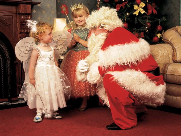 Ein verkleideter Weihnachtsmann und zwei als Christind verkleidete Mädchen in einer gemütlich-rustikalen Umgebung. (Symbolbild)