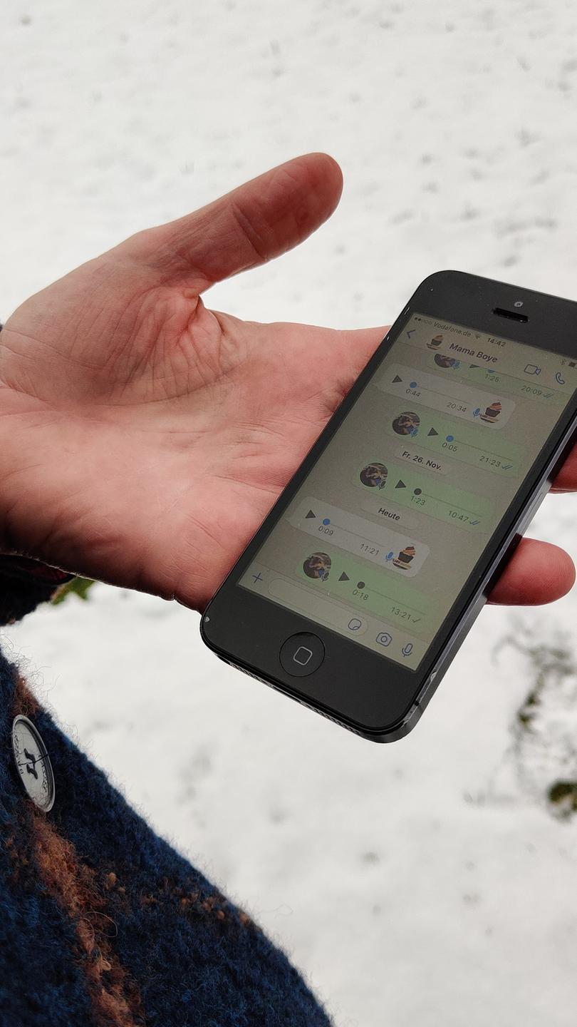 Eine Hand hält ein Smartphone auf der man einen Whatsapp-Chat sehen kann. DIe Person steht auf einer verschneiten Wiese. Eine Hand hält ein Smartphone auf der man einen Whatsapp-Chat sehen kann. DIe Person steht auf einer verschneiten Wiese.