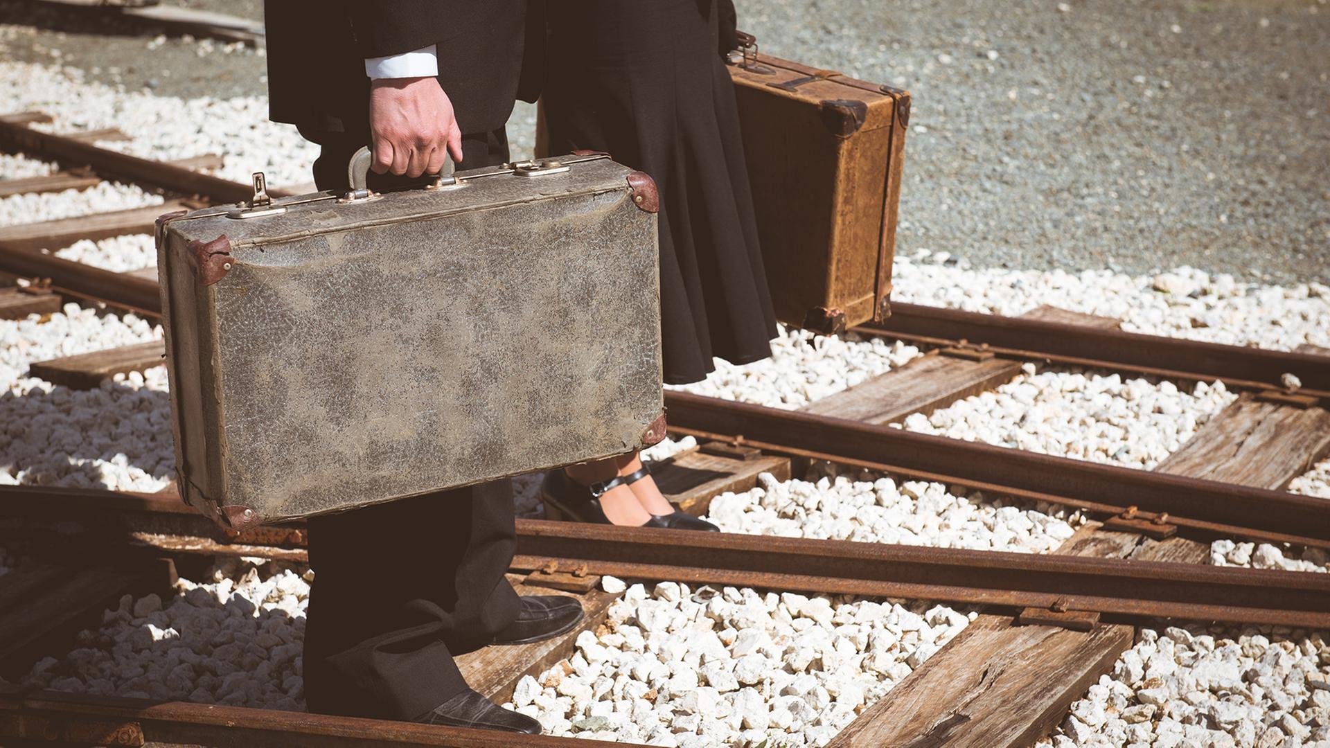 Ein Mann und eine Frau mit je einem Koffer in der Hand, laufen über Bahngleisen. Ein Mann und eine Frau mit je einem Koffer in der Hand, laufen über Bahngleisen.