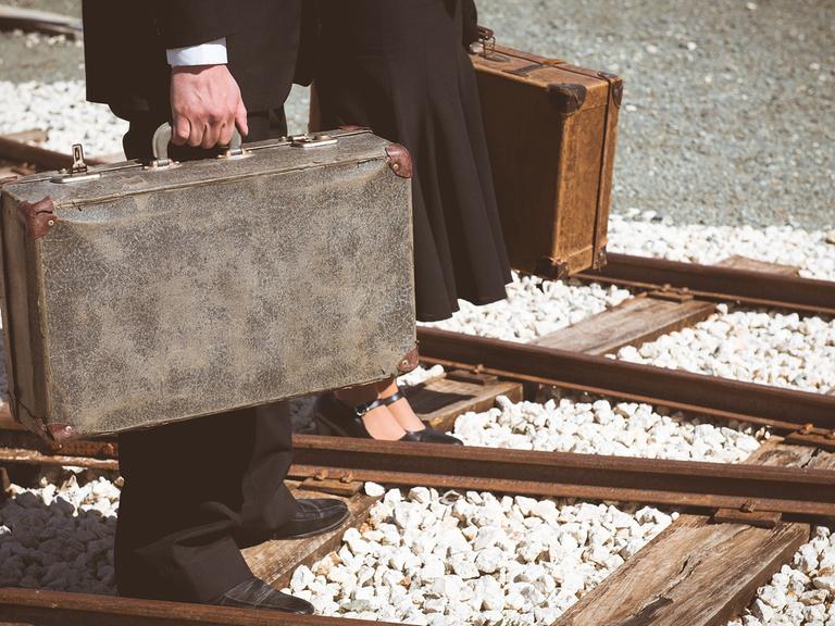 Ein Mann und eine Frau mit je einem Koffer in der Hand, laufen über Bahngleisen. 