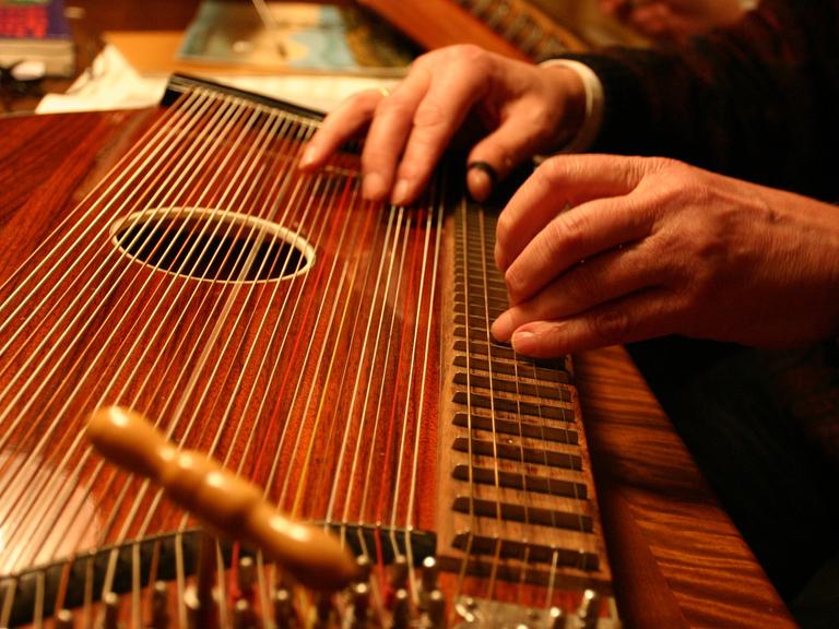 Blick auf zwei Hände, die kundig eine Zither deutscher Bauart spielen.