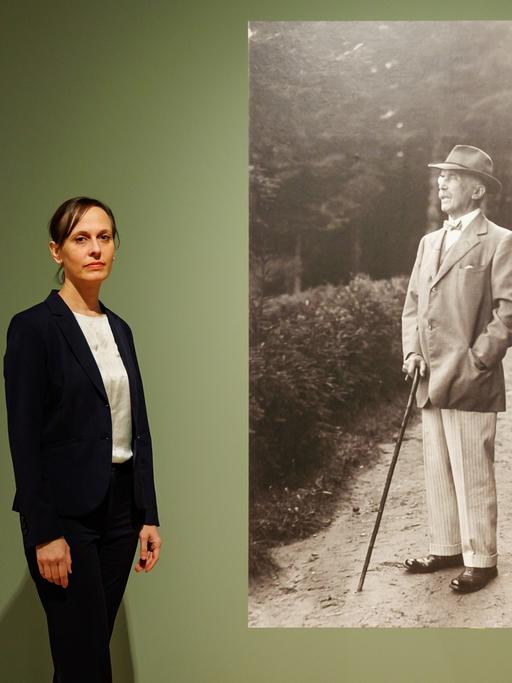 Kuratorin Katharina Weiler steht in der Ausstellung "Die Sammlung Maximilian von Goldschmidt-Rothschilds" neben einem Foto, das Maximilian von Goldschmidt-Rothschild zeigt.  