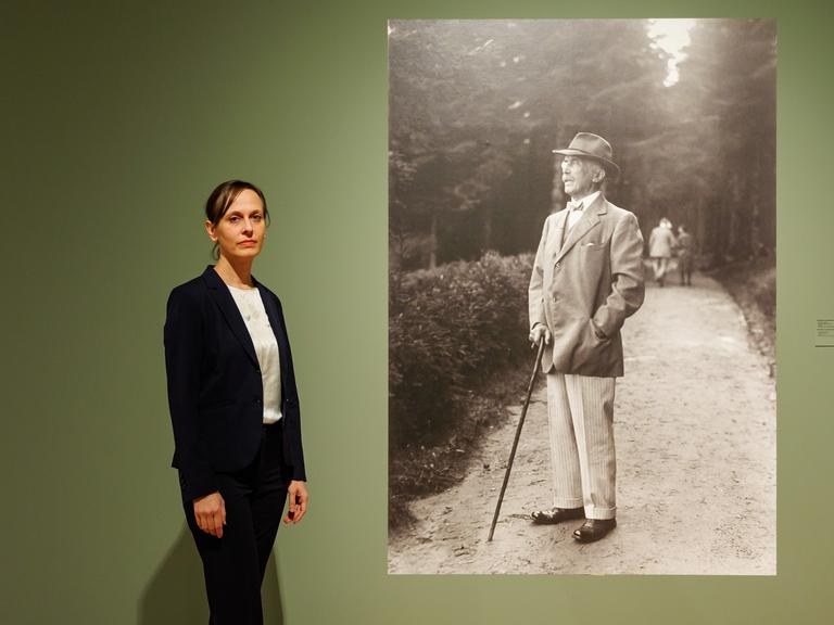 Kuratorin Katharina Weiler steht in der Ausstellung "Die Sammlung Maximilian von Goldschmidt-Rothschilds" neben einem Foto, das Maximilian von Goldschmidt-Rothschild zeigt.  