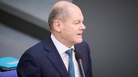 Bundeskanzler Scholz steht im Bundestag hinter einem Mikrofon. Er trägt ein weißes Hemd, eine blaue Krawatte sowie einen dunkelblauen Anzug.