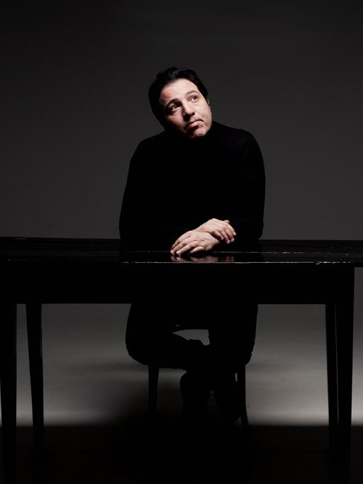 Ein Mann sitzt in einem kahlen Raum an einem Tisch und blickt verträumt an die Decke. 