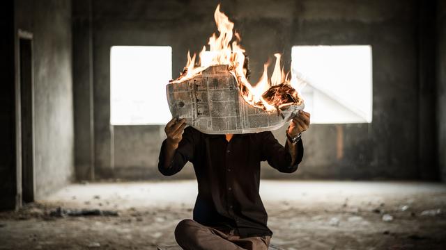 Eine Person hält sich eine brennende Zeitung vor das Gesicht