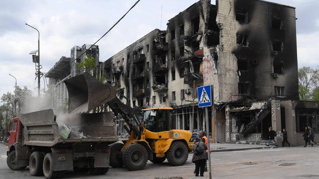 Ein Bagger beläd einen LKW mit Schutt vor einer Häuserruine in Mariupol