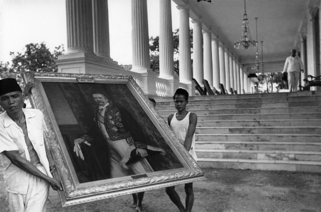 Dua orang Indonesia membawa lukisan cat minyak seorang gubernur Belanda keluar dari istana.