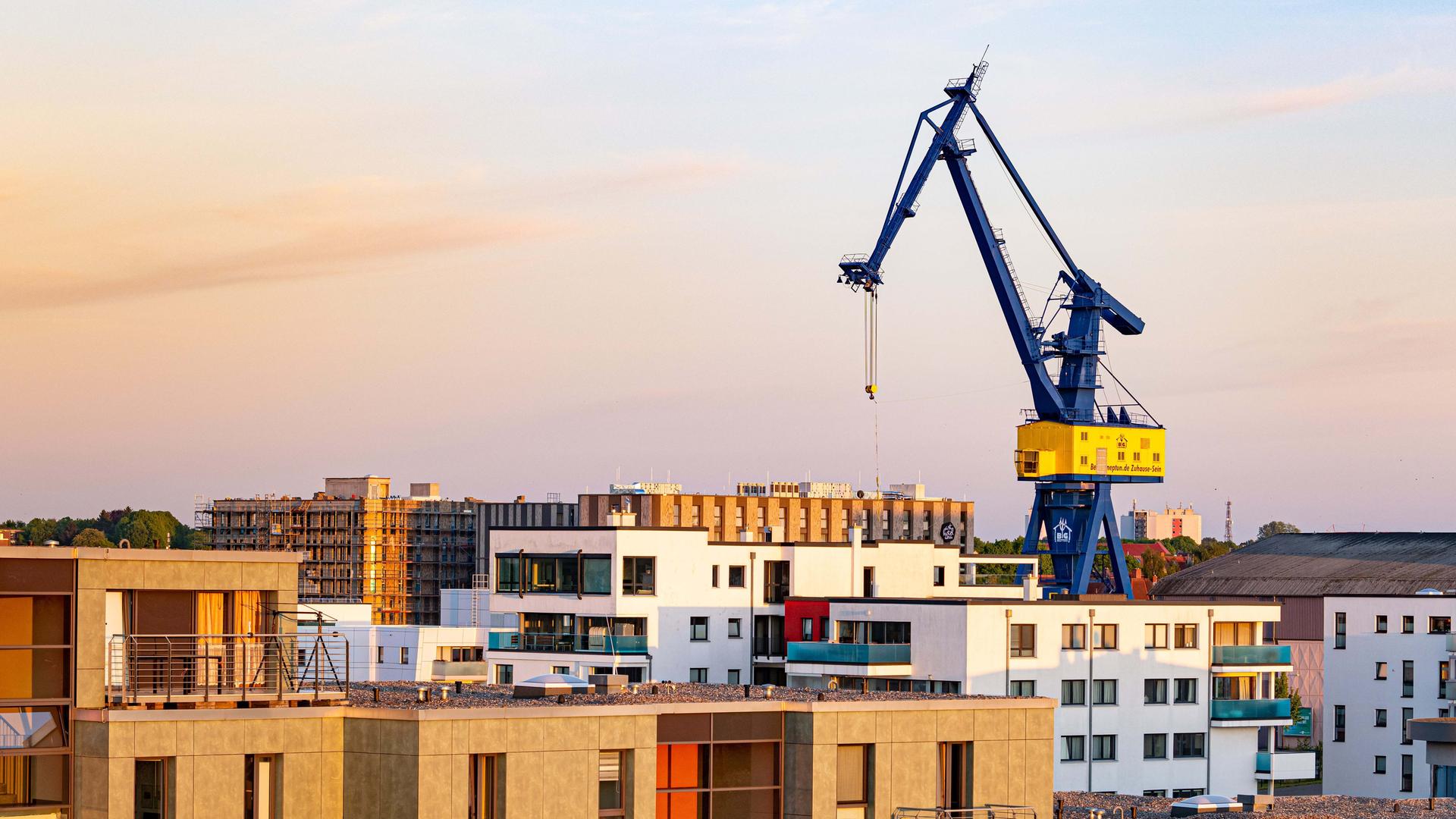 Eine alte, blau gestrichene Krananlage ragt weit über Häuserdächer in Rostock hinaus. Eine alte, blau gestrichene Krananlage ragt weit über Häuserdächer in Rostock hinaus.