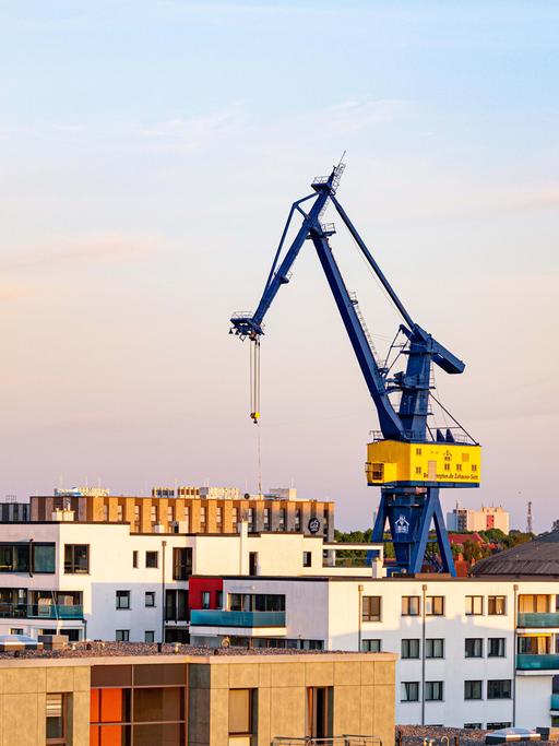 Eine alte, blau gestrichene Krananlage ragt weit über Häuserdächer in Rostock hinaus.