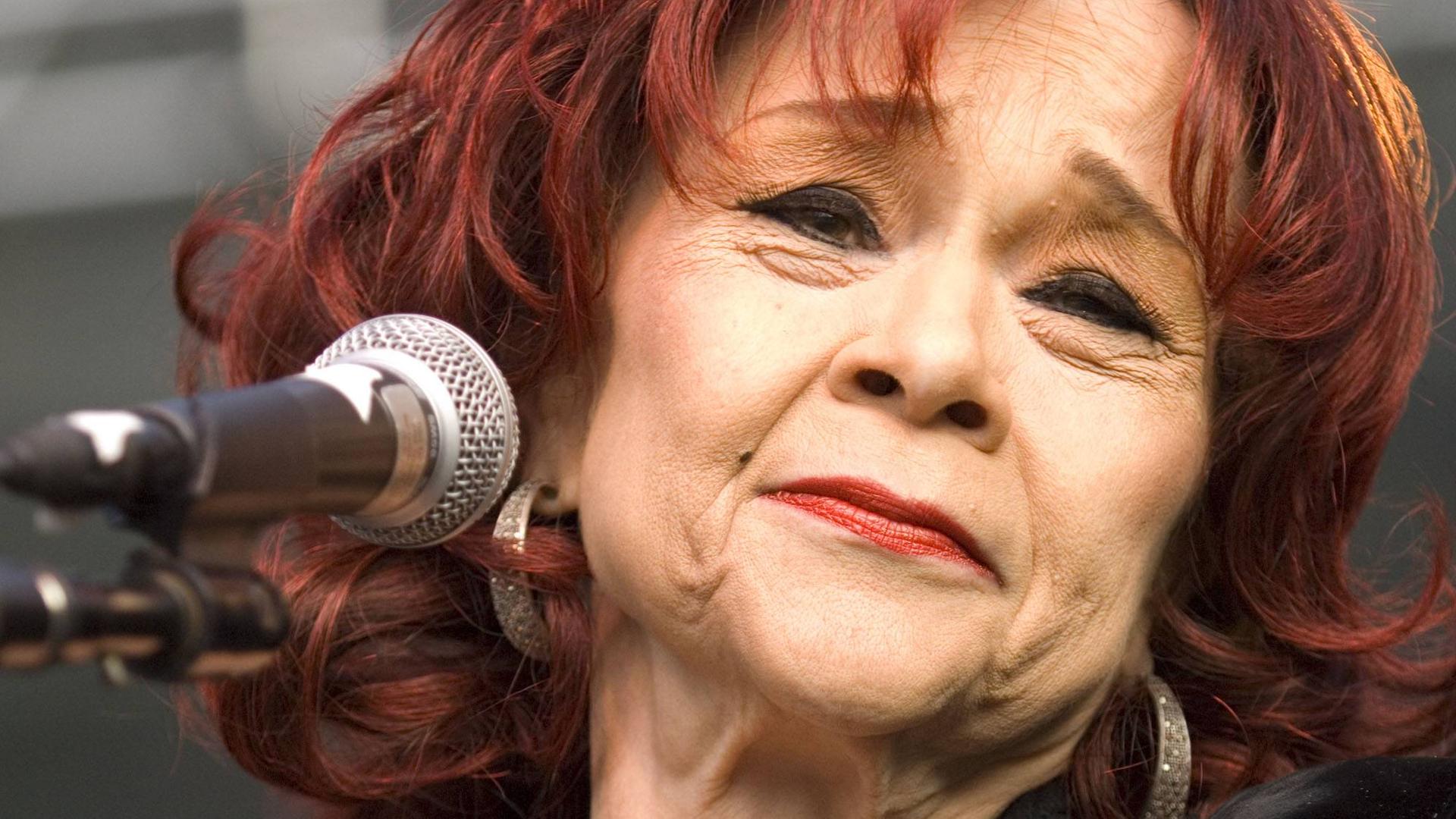 Die Sängerin Etta James bei einem Auftritt. Sie lächelt, neben ihr ist ein Mikrofon. Die Sängerin Etta James bei einem Auftritt. Sie lächelt, neben ihr ist ein Mikrofon.