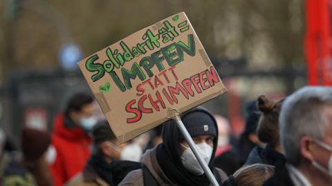Auf einer Demonstration wird ein Schild präsentiert, auf dem steht: "Solidarität = Impfen statt Schimpfen". 