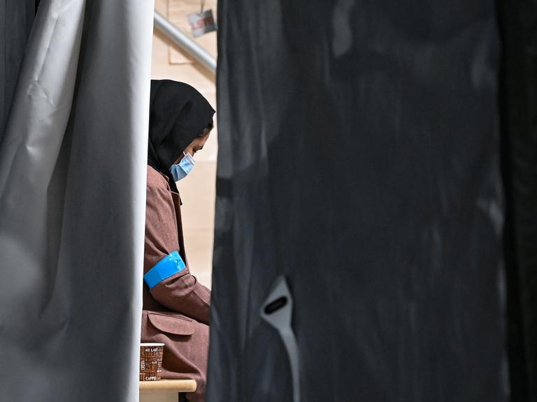 Eine Frau, die zusammen mit weiteren Ortskräften aus Afghanistan auf dem Gelände der DRK-Flüchtlingshilfe in der Erstaufnahmeeinrichtung angekommen ist, sitzt in einem Zelt. 