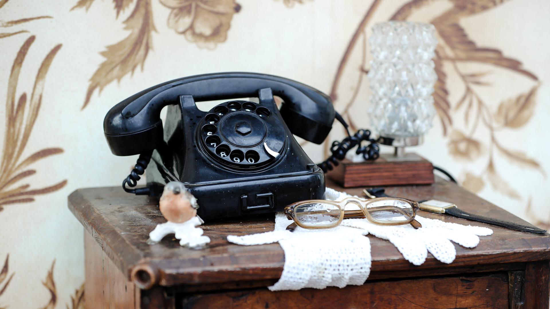 Ein schwarzes, altmodisches Telefon mit Wählscheibe auf einer Kommode mit Spitzendeckchen. Ein schwarzes, altmodisches Telefon mit Wählscheibe auf einer Kommode mit Spitzendeckchen.