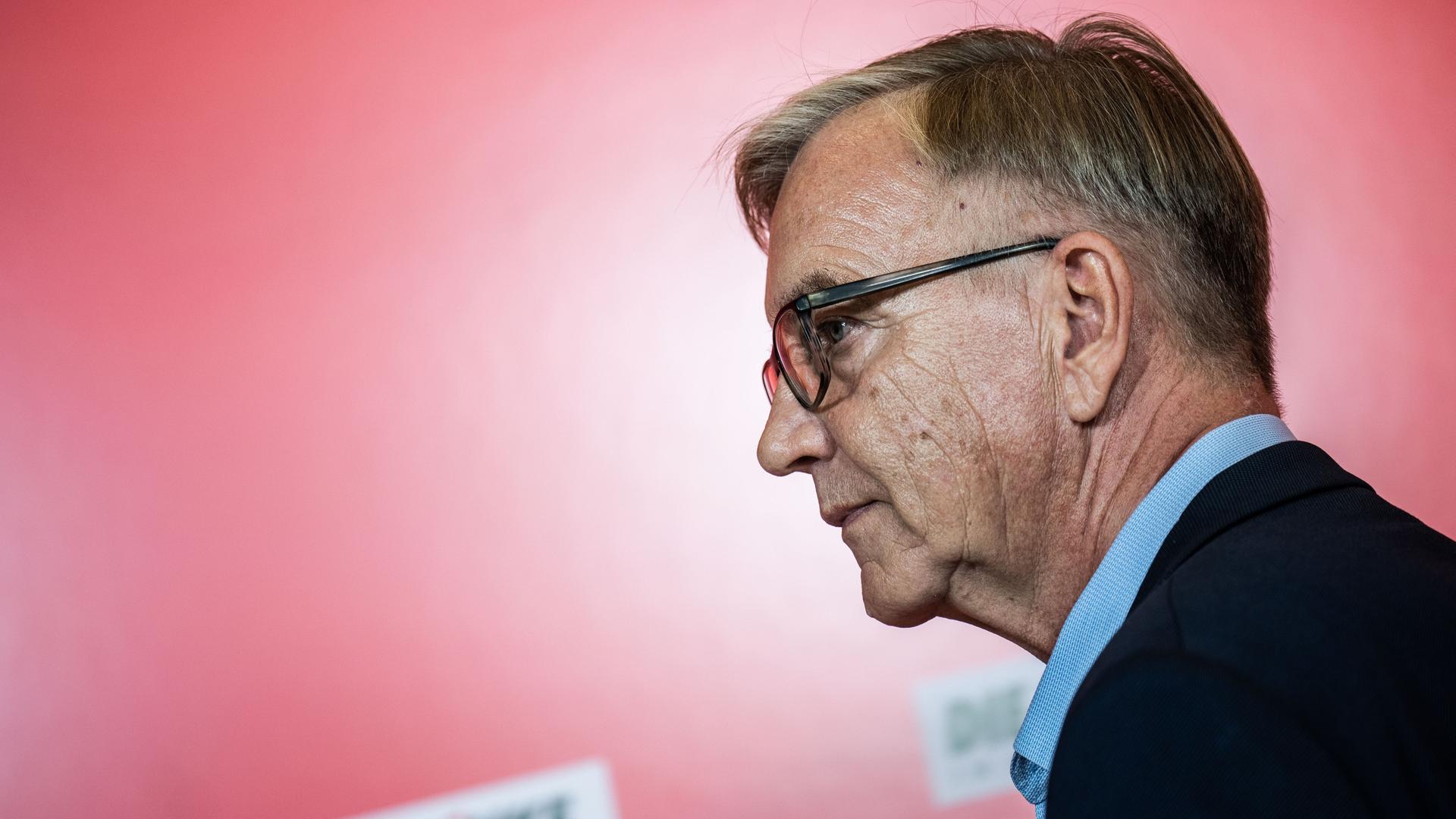 Dietmar Bartsch, Fraktionsvorsitzender der Partei Die Linke, von der Seite fotografiert, vor rotem Hintergrund.