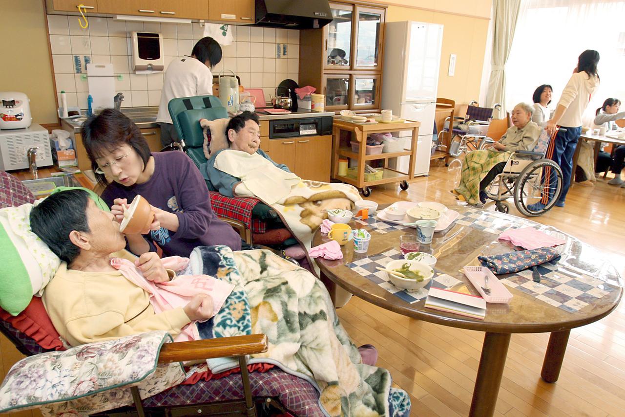 Altenheim in Japan: Menschen sitzen in Rollstühlen in einer Küche und werden gefüttert. Altenheim in Japan: Menschen sitzen in Rollstühlen in einer Küche und werden gefüttert.