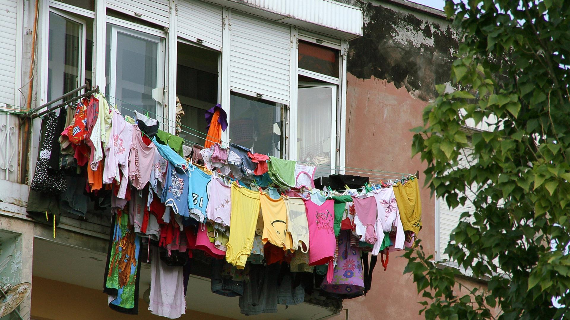 Mehrere Wäscheleinen voll beladen mit bunter Wäsche sind in der Höhe an einem Fenster befestigt.