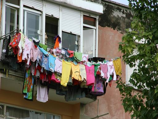 Mehrere Wäscheleinen voll beladen mit bunter Wäsche sind in der Höhe an einem Fenster befestigt.