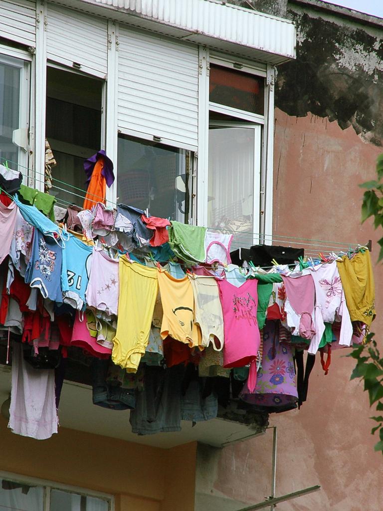 Mehrere Wäscheleinen voll beladen mit bunter Wäsche sind in der Höhe an einem Fenster befestigt.