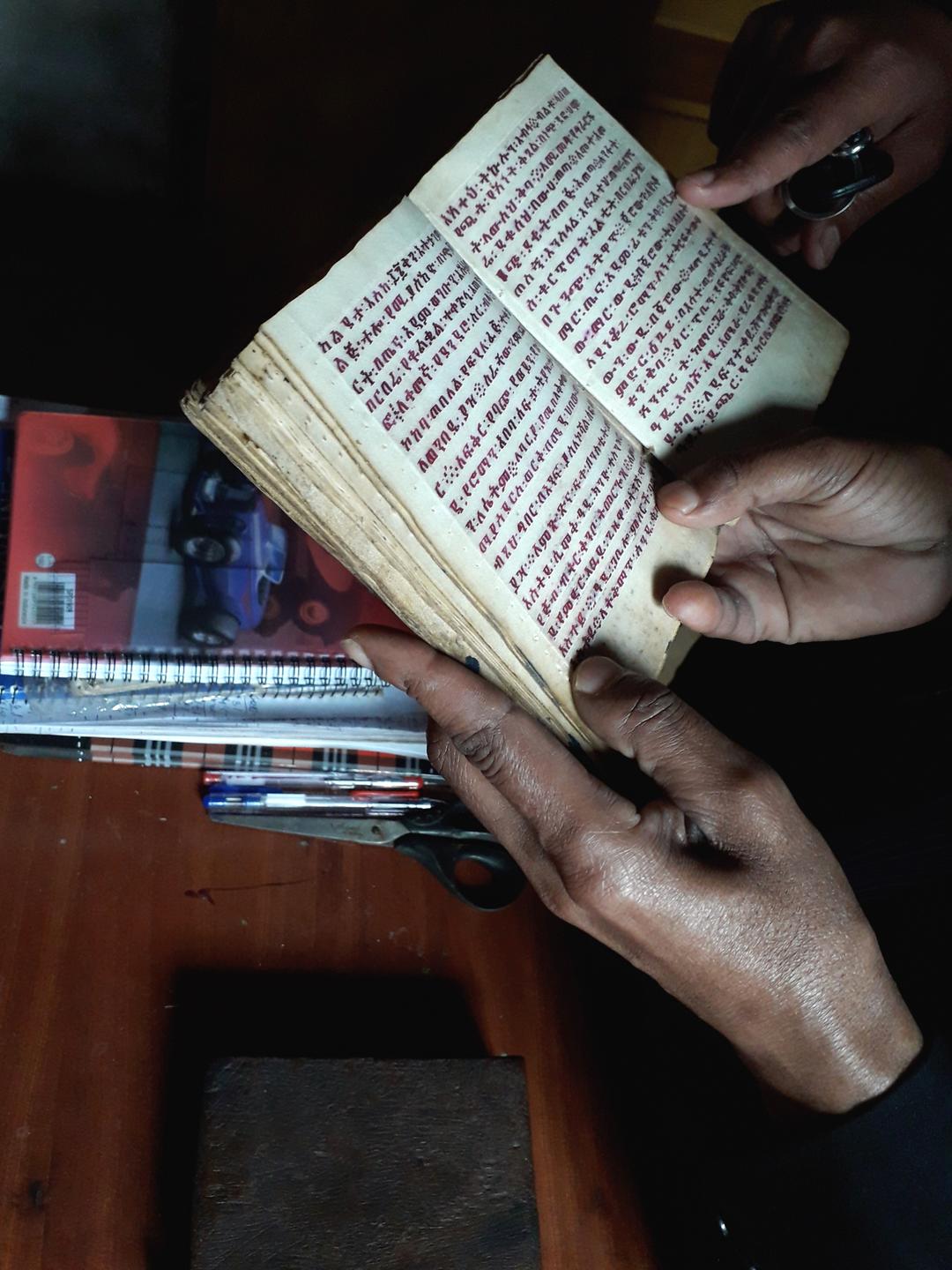 Heiler Tegistu hält ein kleines Buch aufgeklappt in seinen Händen. Heiler Tegistu hält ein kleines Buch aufgeklappt in seinen Händen.