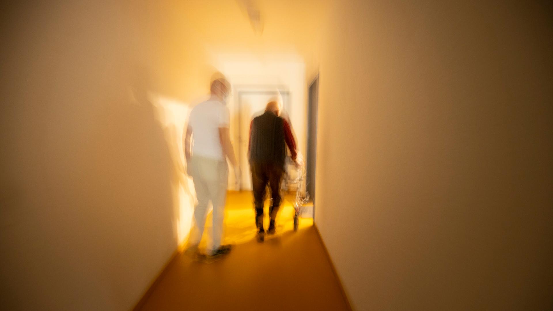 Pfleger und Mann mit Rollator in einem dunklen Flur. Pfleger und Mann mit Rollator in einem dunklen Flur.