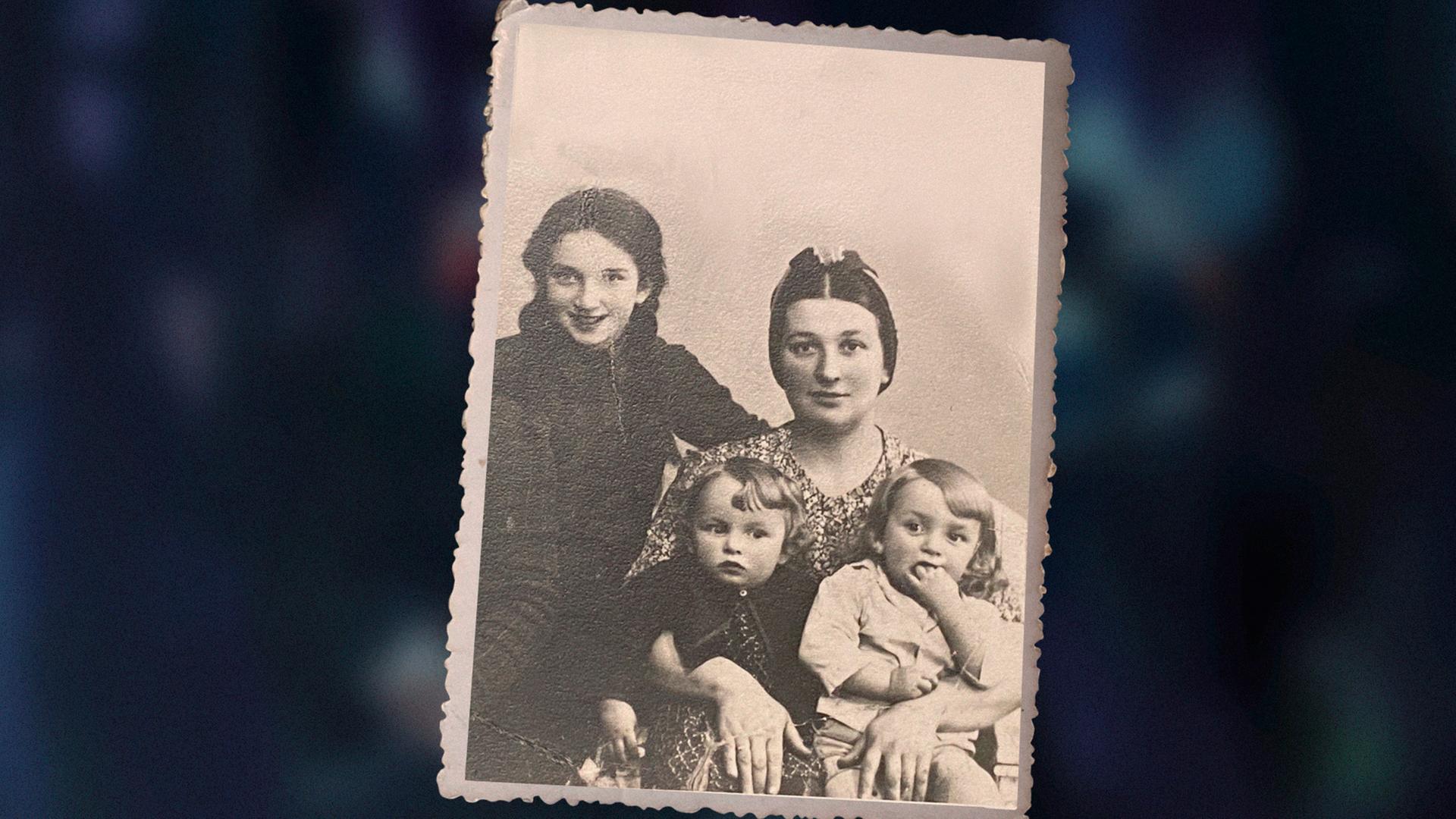 Das Bild zeigt eine alte, schwarzweiße Familienfotografie aus den frühen 1940er . Sie zeigt die dreijährigen Zwillinge Ida und Adam Paluch im Arm ihrer Mutter. Links im Bild ist ihre ältere Schwester Genia zu sehen. 