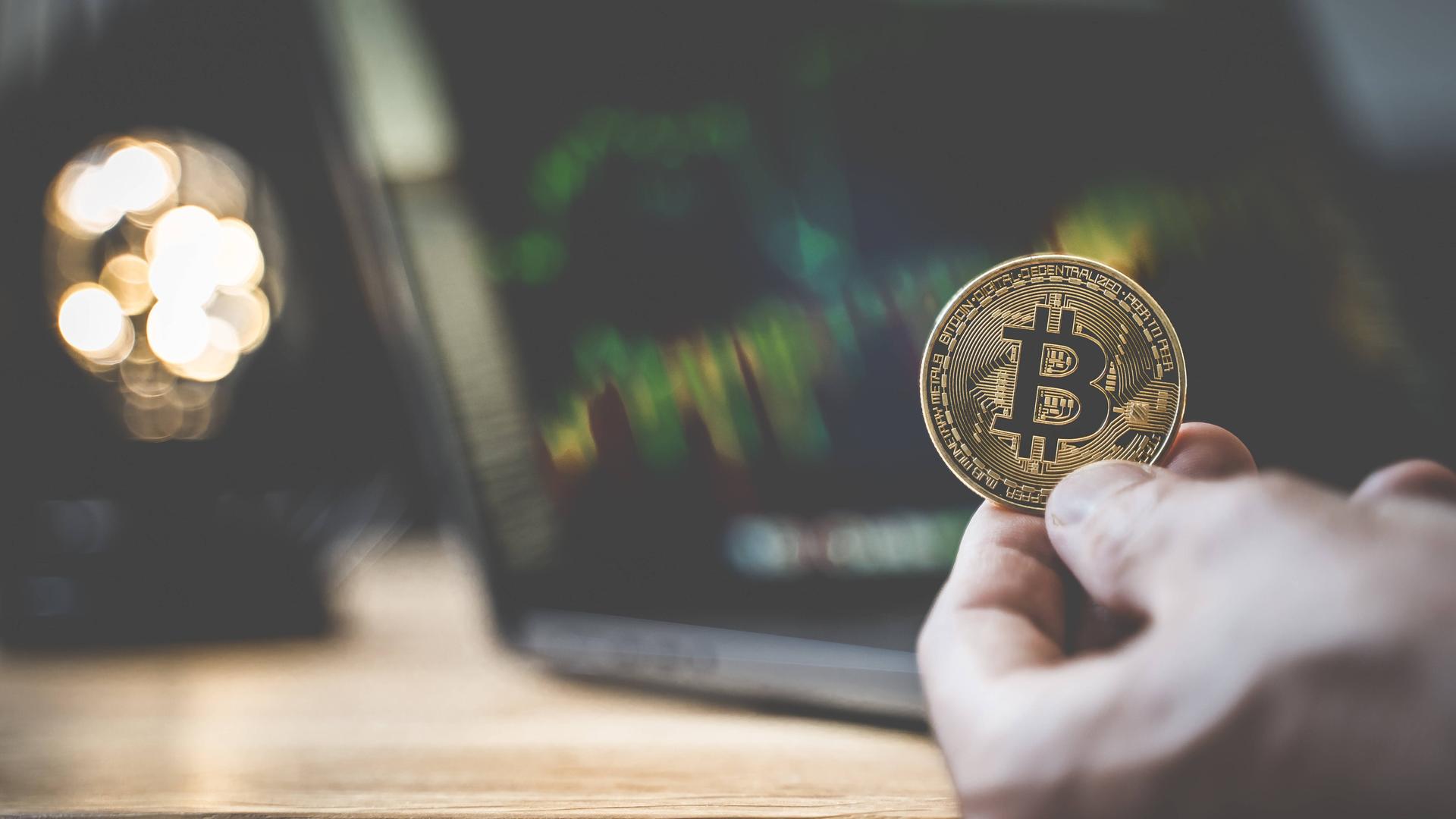Eine physische goldene Bitcoin vor einem Computermonitor Eine physische goldene Bitcoin vor einem Computermonitor