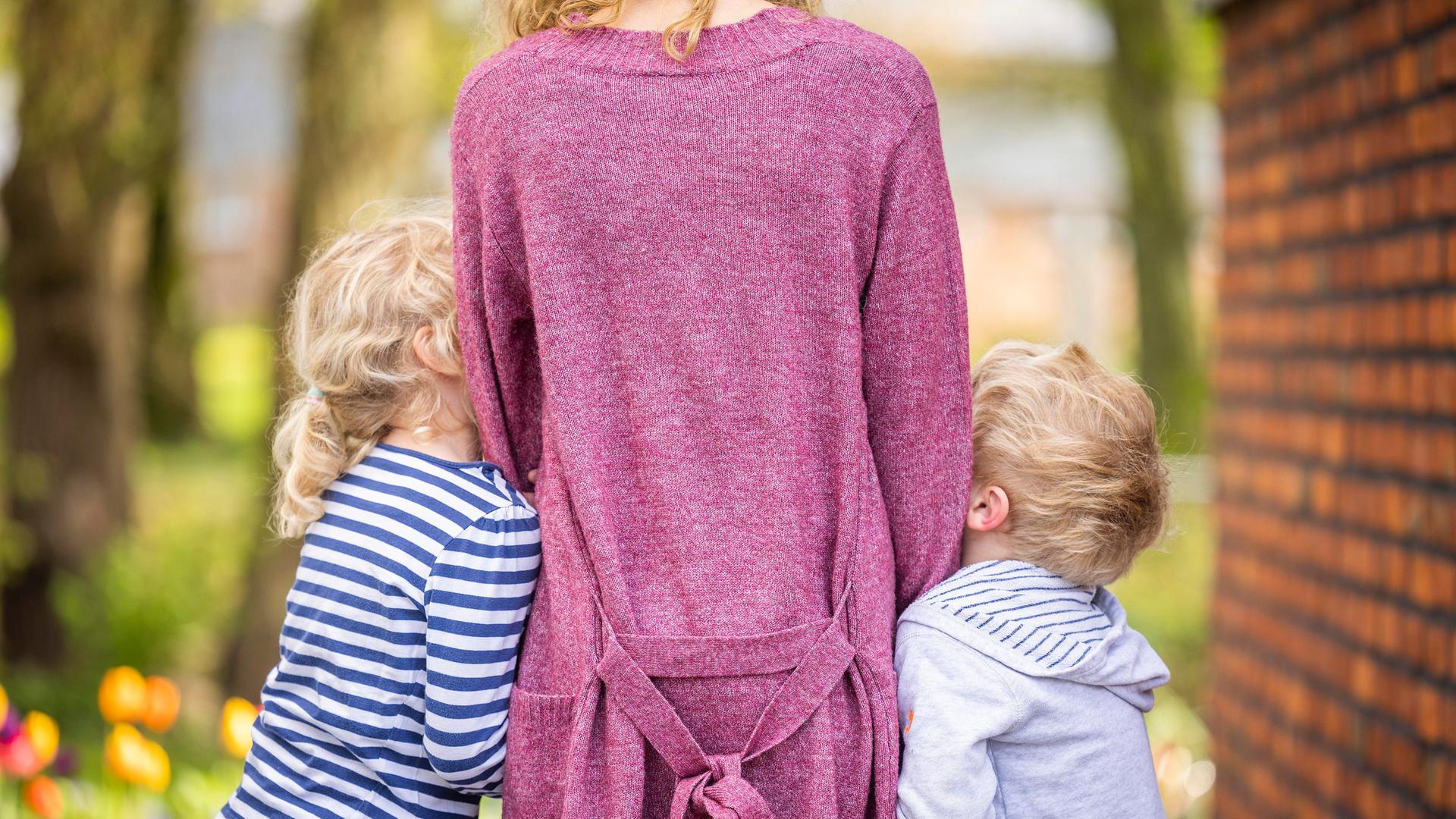 Zu sehen ist eine Frau von hinten, an die sich jeweils ein Junge und ein Mädchen anschmiegen. Vermutlich Sohn und Tochter. Zu sehen ist eine Frau von hinten, an die sich jeweils ein Junge und ein Mädchen anschmiegen. Vermutlich Sohn und Tochter.