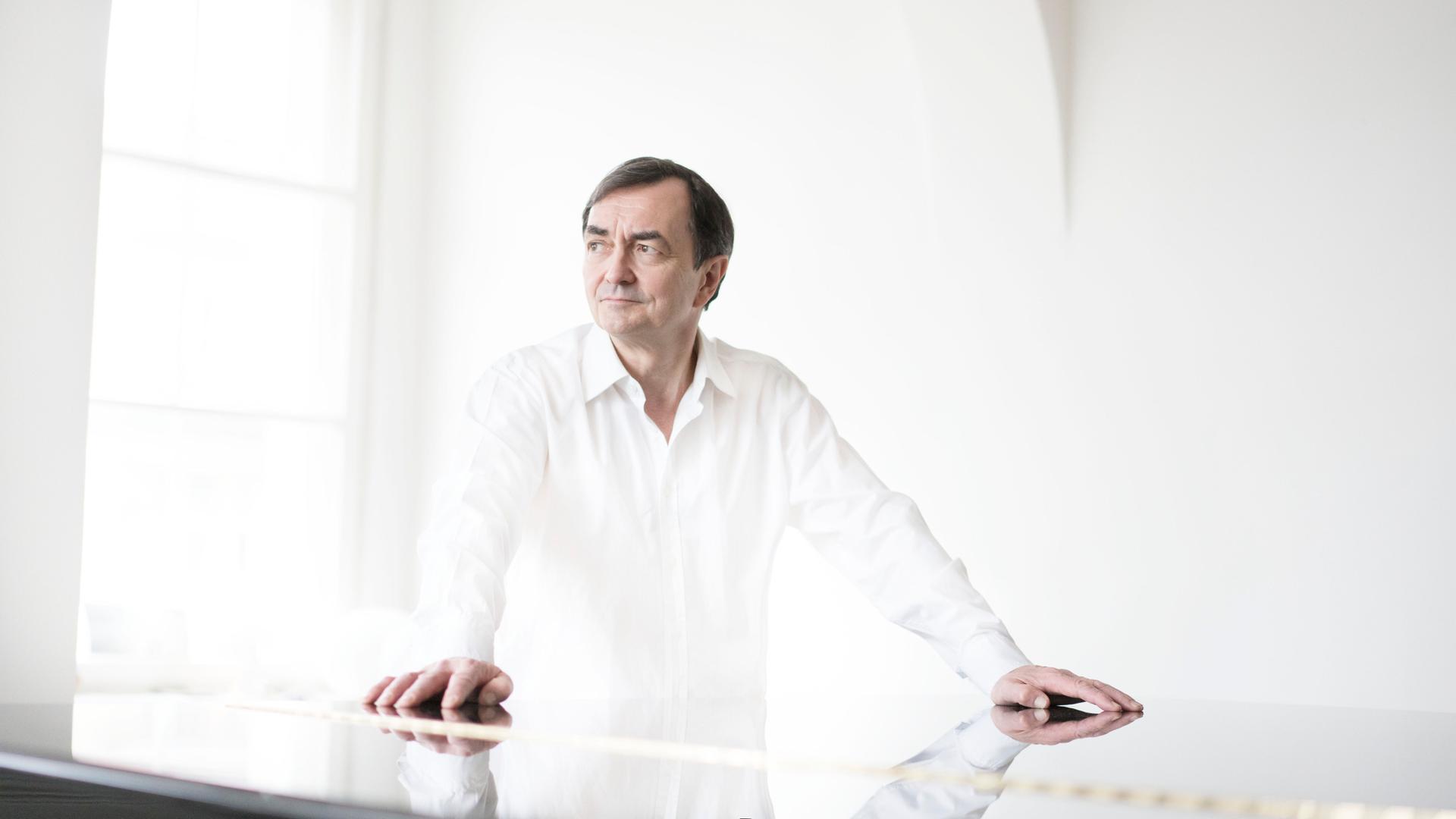 Der ganz in weiß gekleidete Pianist steht in einem weißen Raum mit großem Fenster und hat beide Arme auf einen geschlossenen Flügel gestützt. Der ganz in weiß gekleidete Pianist steht in einem weißen Raum mit großem Fenster und hat beide Arme auf einen geschlossenen Flügel gestützt.