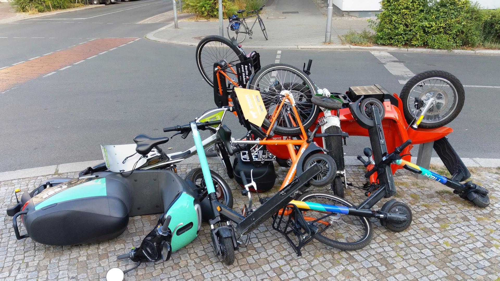 Elekto-Roller, E-Tretroller sowie Leihräder liegen von Unbekannten aufeinandergetürmt an einer Kreuzung in Berlin-Schöneberg auf dem Bürgersteig. Elekto-Roller, E-Tretroller sowie Leihräder liegen von Unbekannten aufeinandergetürmt an einer Kreuzung in Berlin-Schöneberg auf dem Bürgersteig.