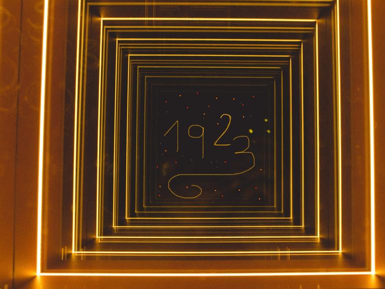 Blick durch eine Art beleuchteter Gang, der zu einem Quadrat führt, in dem die Jahreszahl 1923 steht.