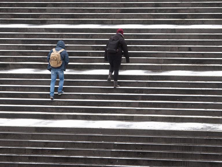 Passanten gehen über eine leicht verschneite Treppe am Raschplatz in der Innenstadt von Hannover.
