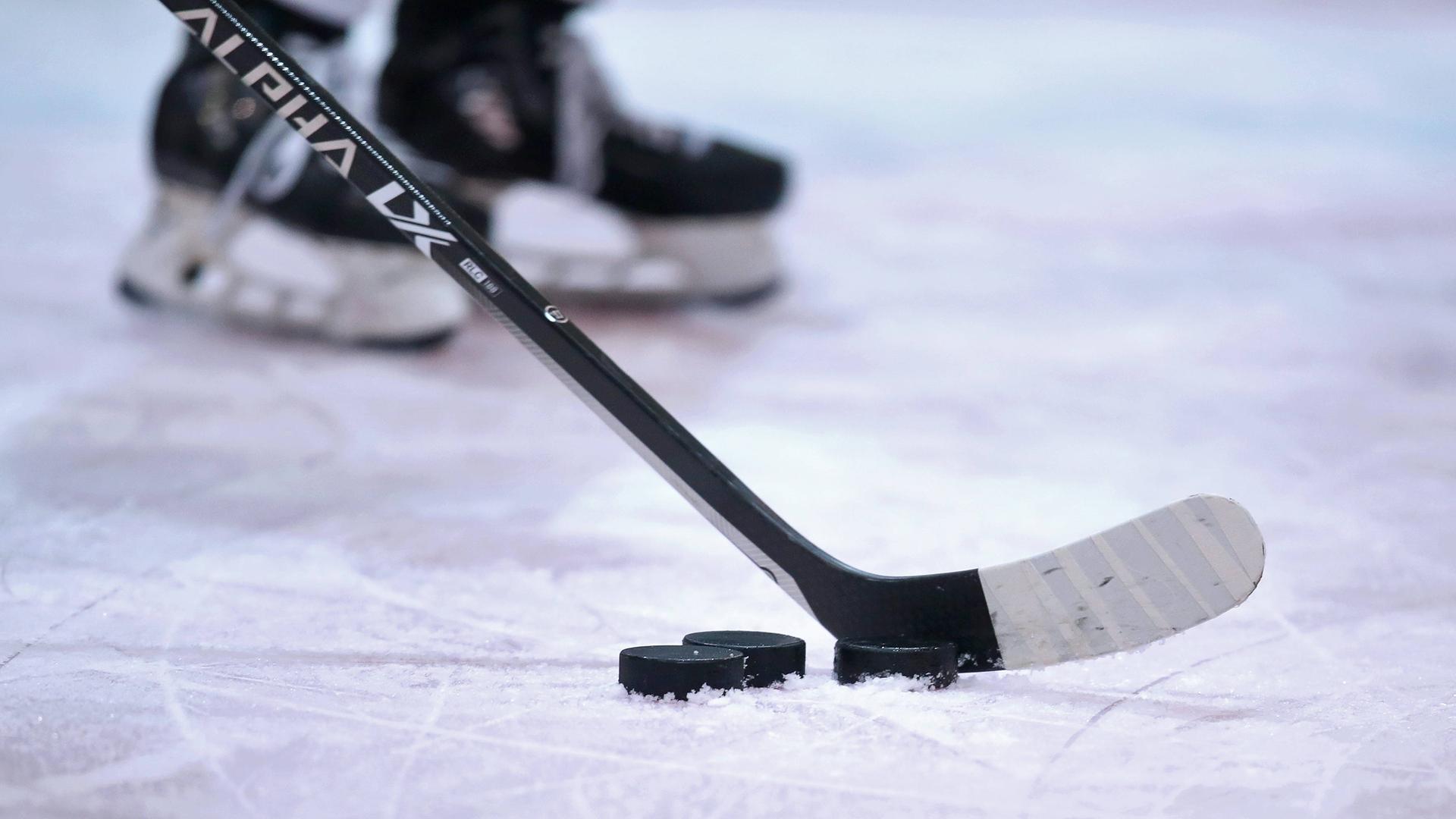 Ein Eishockeyschläger vor einem Puk auf dem Eis. Dahinter verschwommen ein paar Schlittschuhe. Ein Eishockeyschläger vor einem Puk auf dem Eis. Dahinter verschwommen ein paar Schlittschuhe.