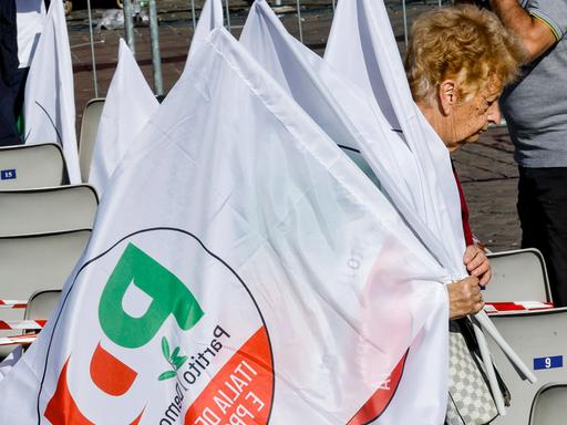 Die Partito Democratico beendet ihren Wahlkampf. Eine Frau sammelt gebeugt die Fahnen ein nach einer der letzten Wahlkampfveranstaltungen in Rom.