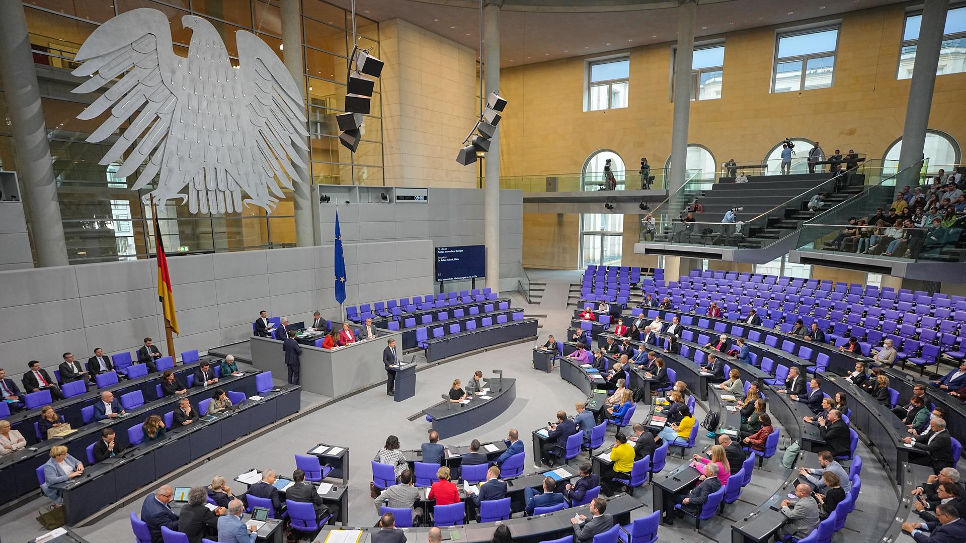 Der Plenarsaal des Bundestags: An der Wand hängt der Bundesadler, Abgeordnete sitzen auf den blauen Bundestagsstühlen.