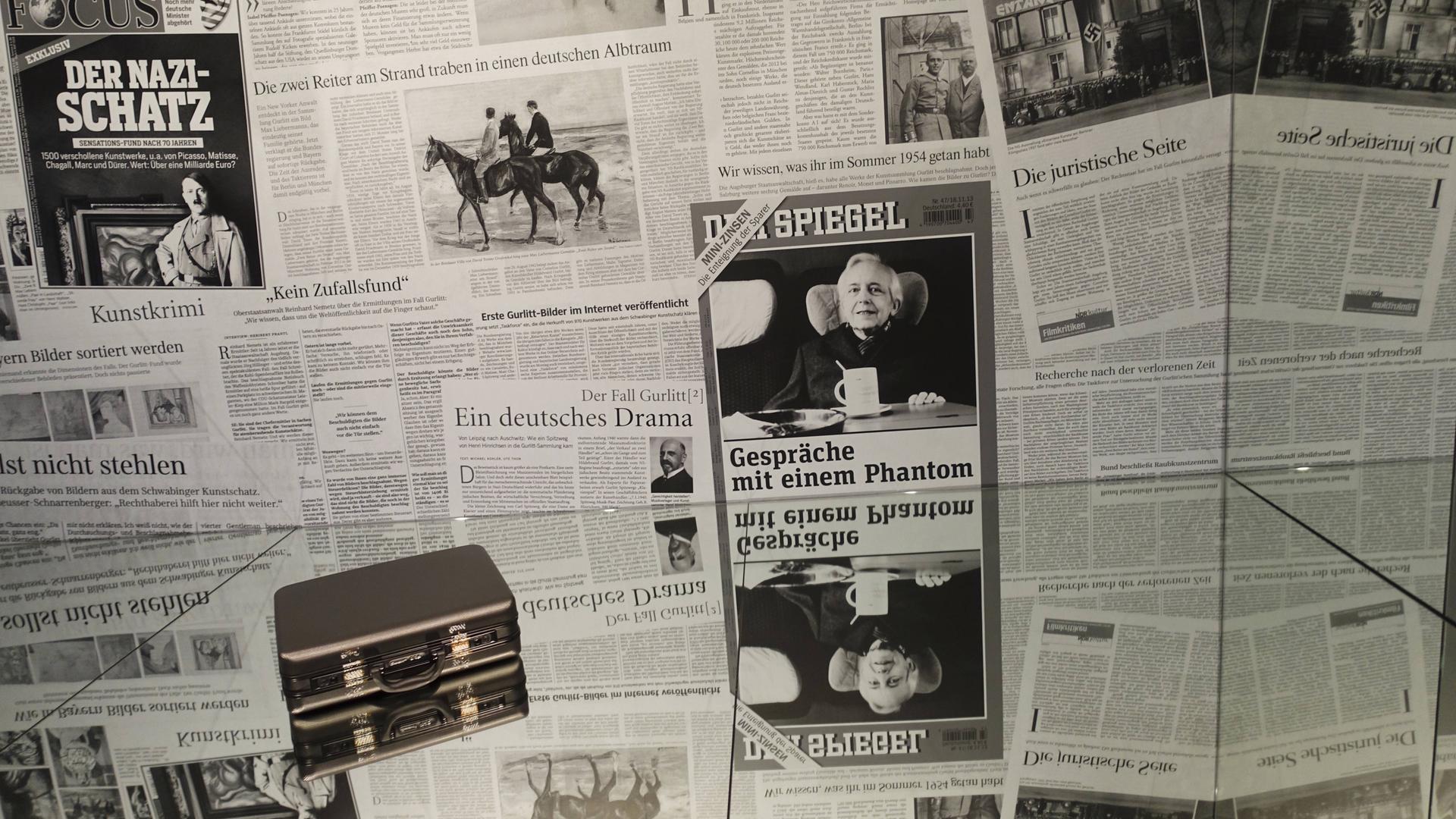 Das Bild zeigt eine Collage aus Zeitungsberichten und einen Original-Koffer Gurlitts aus der Ausstellung "Bestandsaufnahme Gurlitt" im Gropius-Bau von 2018. 
