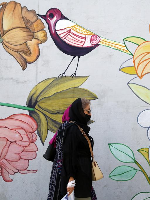 Eine Frau mit Kopftuch läuft an einem Wandbild mit Blumen und Vogel in einer Straße in Teheran vorbei.