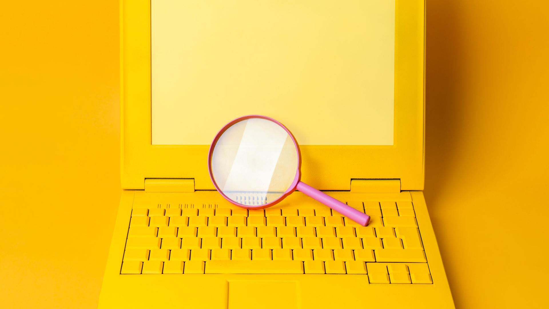 Ein gelber Laptop mit einer Lupe vor gelbem Hintergrund. Ein gelber Laptop mit einer Lupe vor gelbem Hintergrund.
